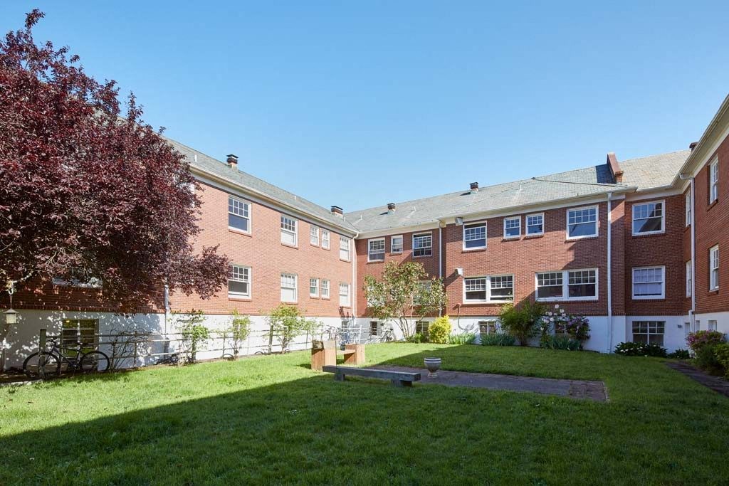a grassy area with a fence in front of a brick building at MILEPOST 5 Apartments, Oregon, 97213