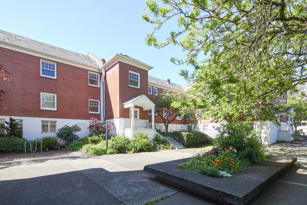 brick building with a white porch and a tree in front of it at MILEPOST 5 Apartments, Oregon, 97213