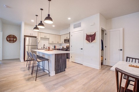 an open kitchen and dining room with a large island and a stainless steel refrigerator