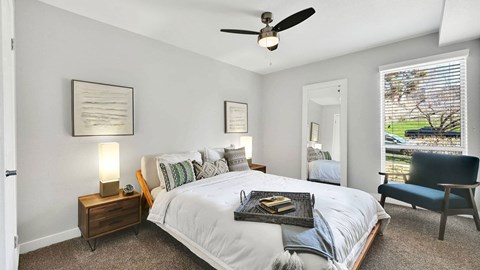 A bedroom with a large bed, a ceiling fan, and a chair.