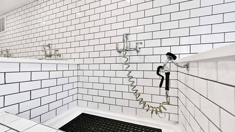 A white tiled shower with a black drain.