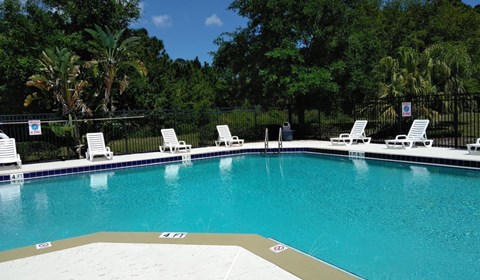 A pool with white chairs and a blue sky in the background.