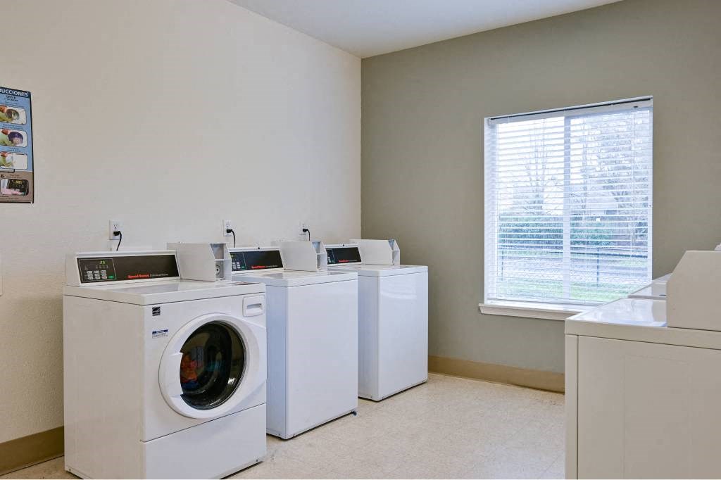 a laundry room with four washing machines and a window at Quail Run Apartments, Vancouver