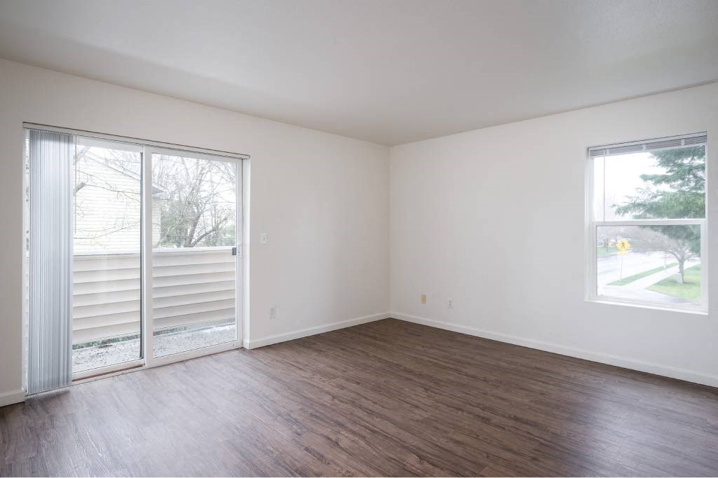 an empty living room with wood floors and a sliding glass door at Quail Run Apartments, Vancouver, Washington
