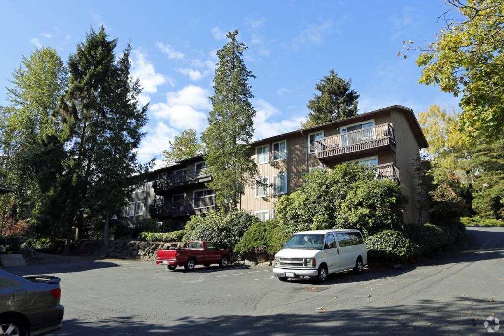 an apartment building with cars parked in a parking lot at Whisperwood, Seattle, 98168