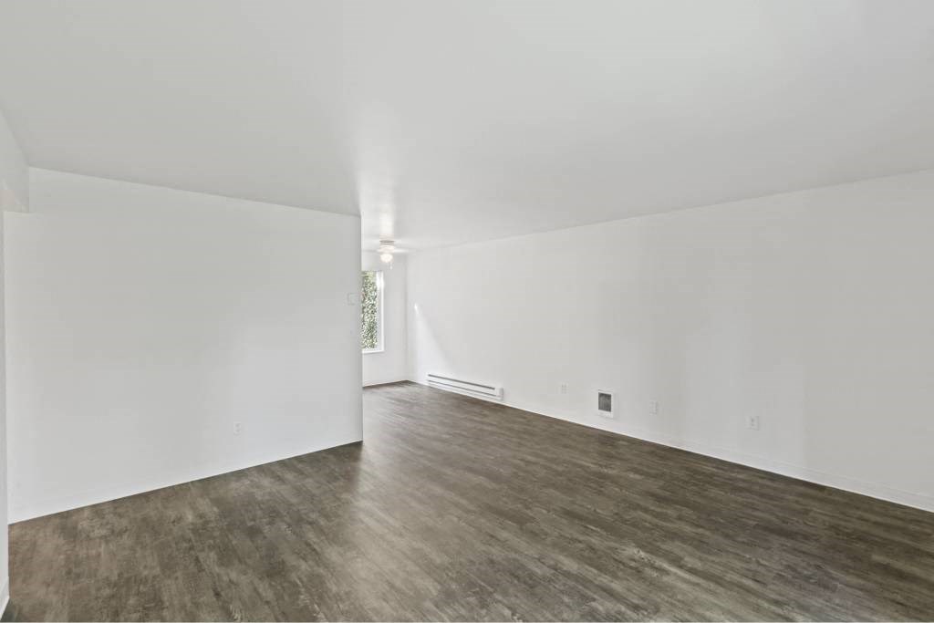 an empty living room with white walls and wood floors at Whisperwood, Seattle, WA 98168
