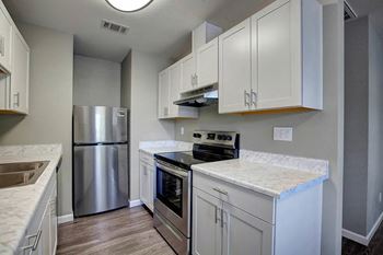 A kitchen with white cabinets and a stainless steel refrigerator at The Henley Apartments, Suisun City, California