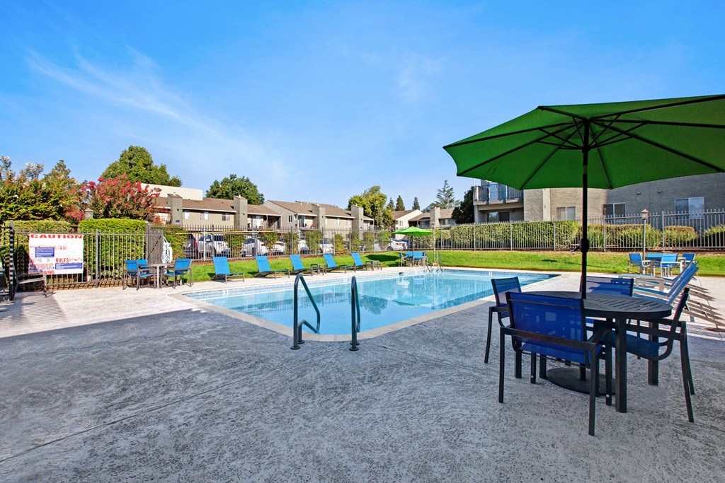 A green umbrella is on a table next to a pool at The Henley Apartments, California, 94585