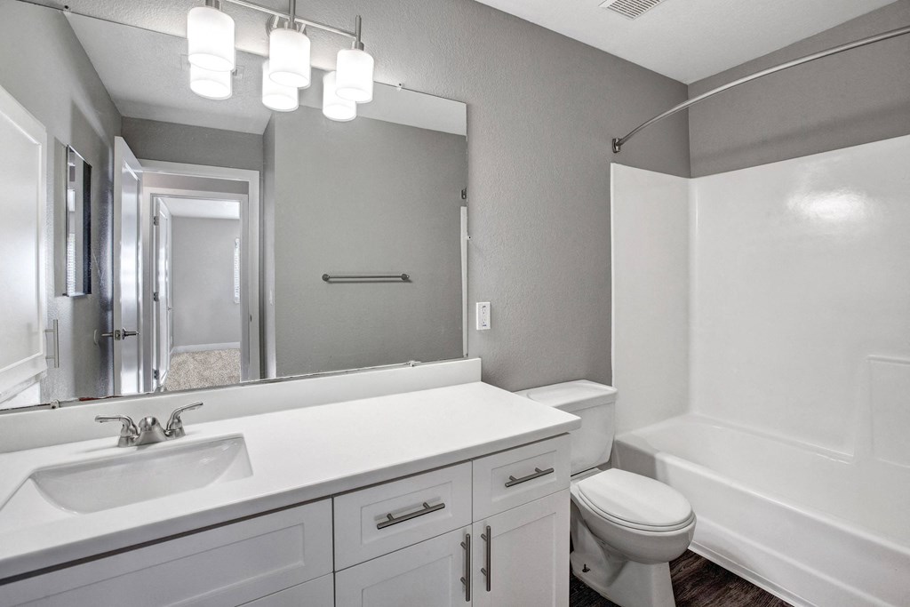 A white bathroom with a sink, mirror, toilet and bathtub at The Henley Apartments, Suisun City