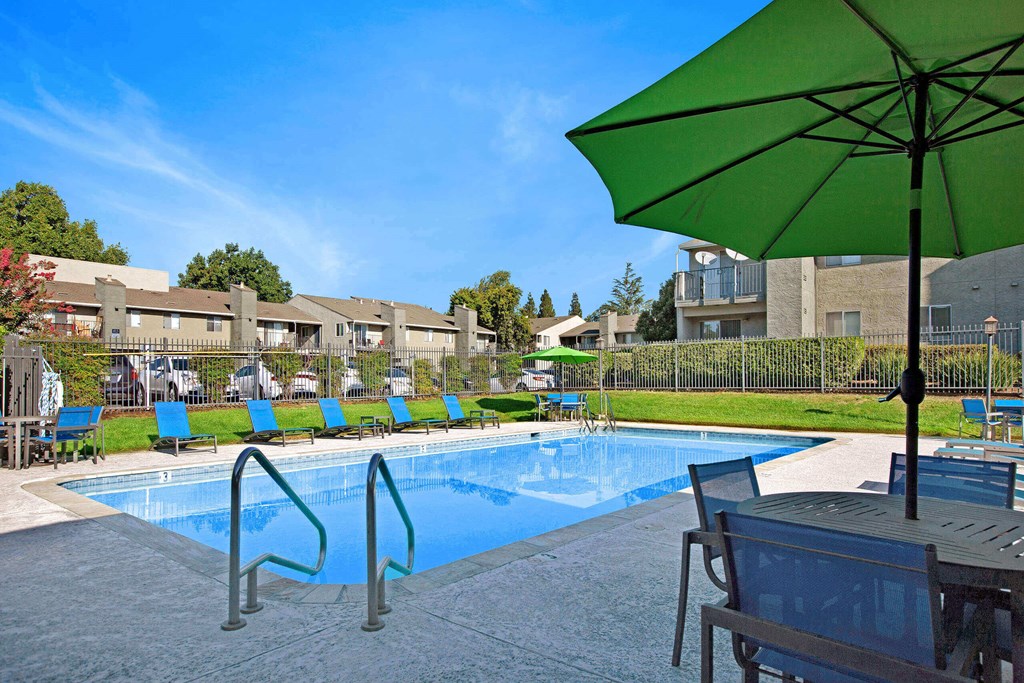 A green umbrella is next to a pool at The Henley Apartments, Suisun City, CA, 94585