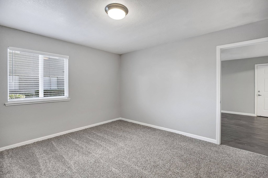 A room with a carpeted floor, a window with blinds, and a door at The Henley Apartments, Suisun City, 94585