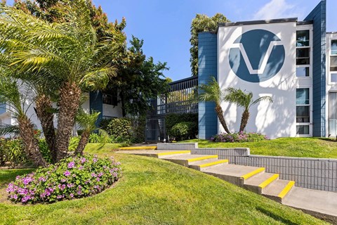 A building with a logo on it is surrounded by a green lawn and palm trees.