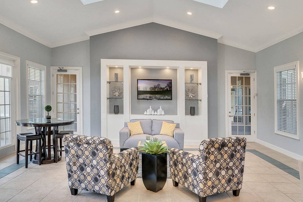 A living room with a patterned chair and a television on the wall at The Villages on Millenia Apartments, Orlando 32839