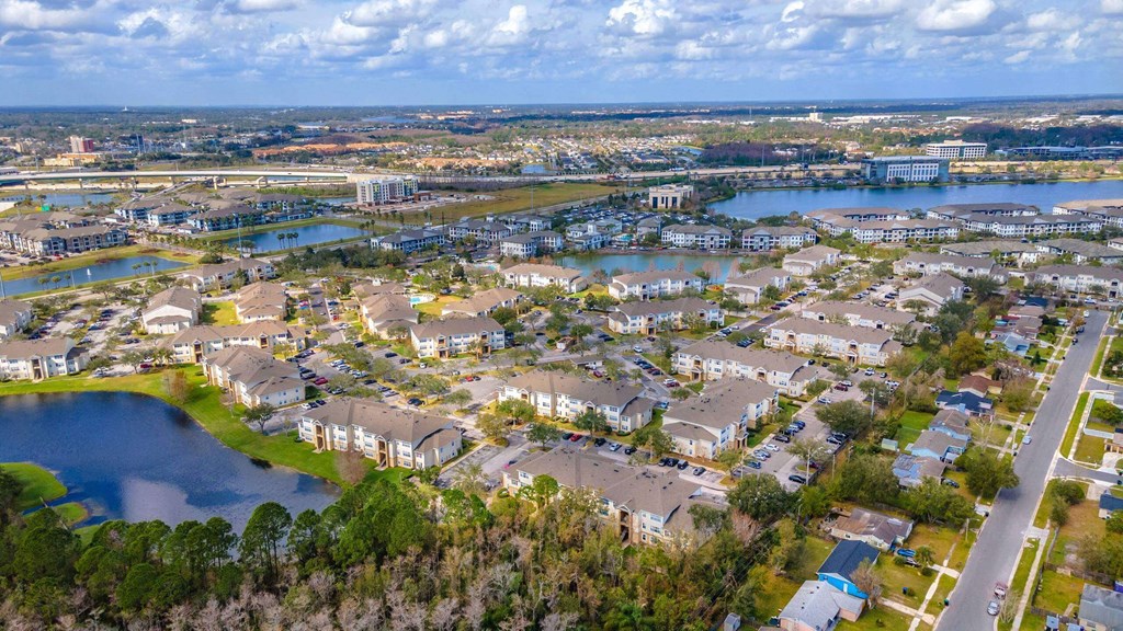 A bird's eye view of a residential area with houses, a lake, and a bridge in the distance at The Villages on Millenia Apartments, Orlando