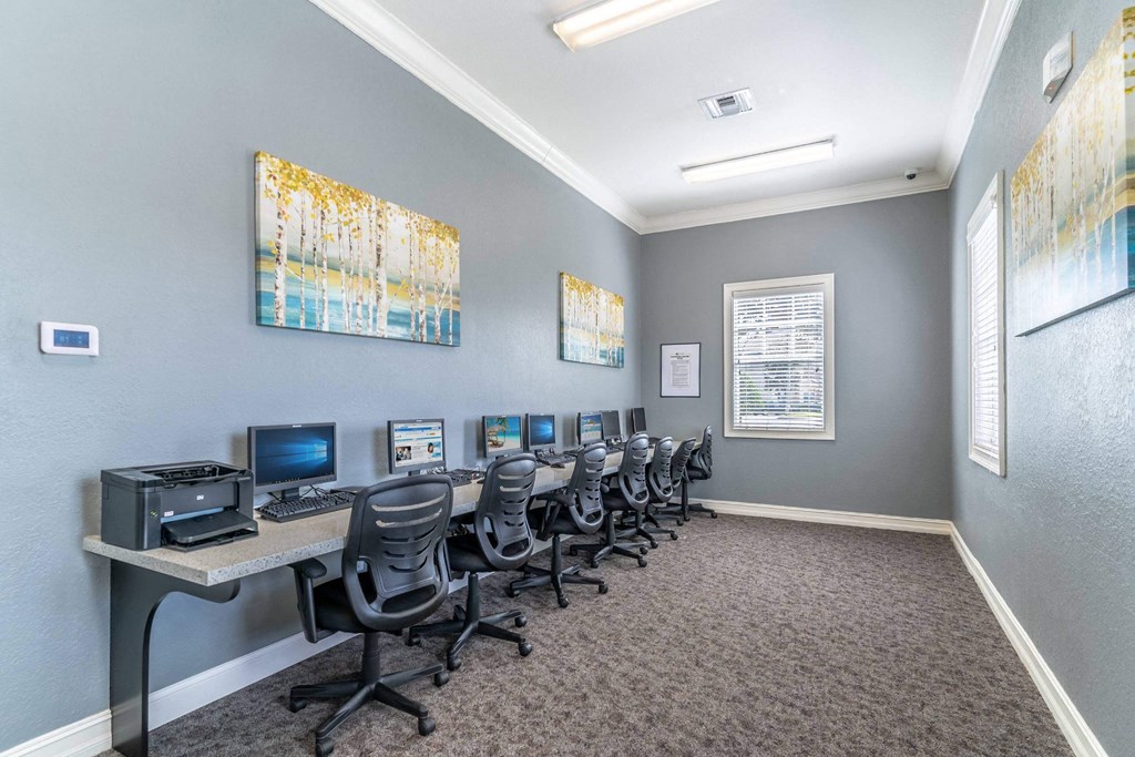 A room with grey walls and a carpeted floor has a row of chairs and desks with computers on them at The Villages on Millenia Apartments, Orlando
