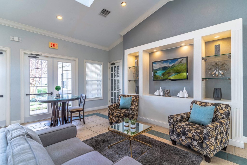 A living room with a grey couch, a patterned armchair, and a television mounted on the wall at The Villages on Millenia Apartments, Florida
