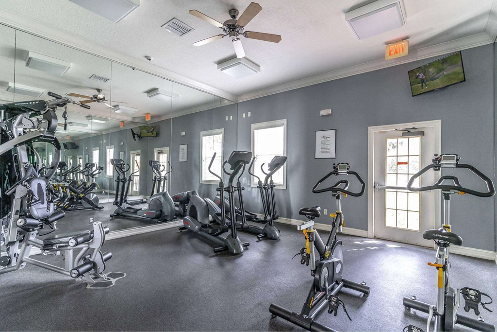 A gym with a variety of exercise equipment including treadmills, stationary bikes, and weight machines at The Villages on Millenia Apartments, Orlando, Florida