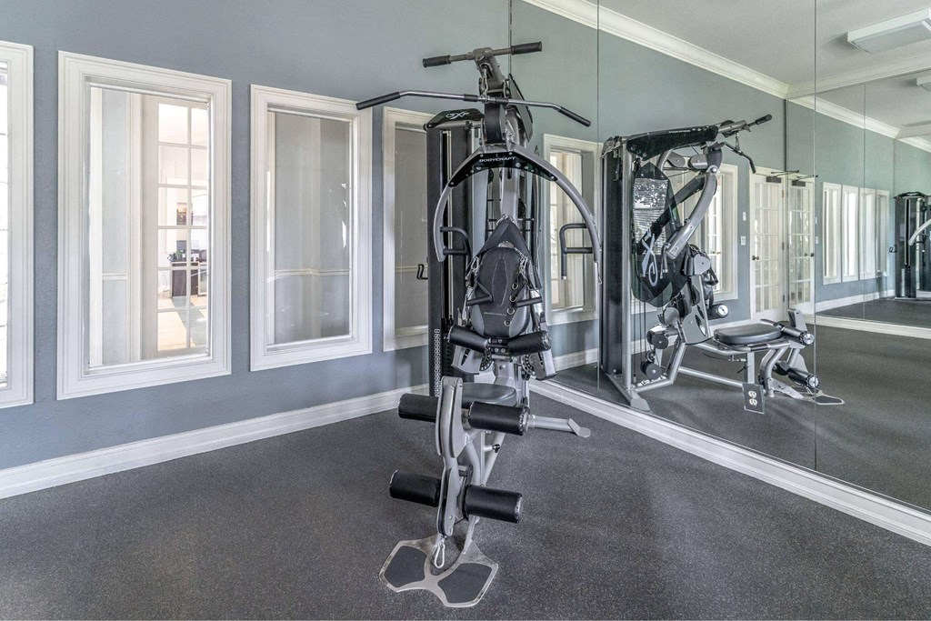 A well-equipped gym with a mirrored wall and various exercise machines at The Villages on Millenia Apartments, Orlando, FL, 32839
