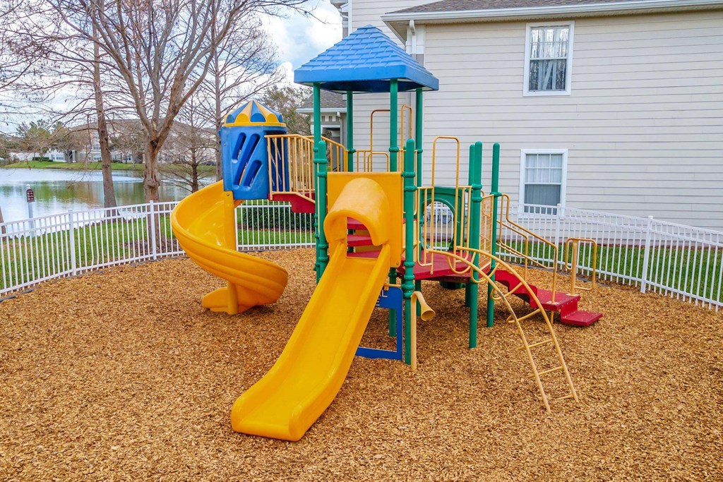A playground with a yellow slide and a blue roofed structure at The Villages on Millenia Apartments, Orlando, FL, 32839