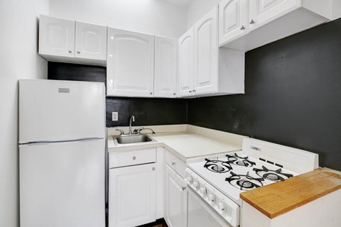 A white refrigerator is in a kitchen with white cabinets and a white stove.