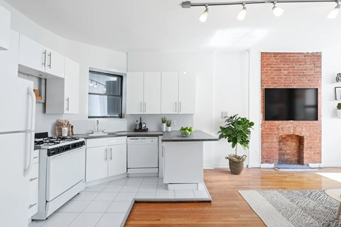 A modern kitchen with white cabinets and a brick fireplace.