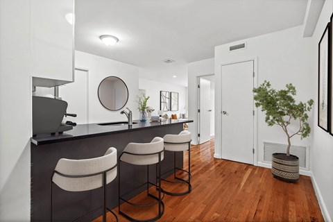 A kitchen with white walls and a black counter top with three bar stools.
