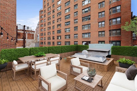 A patio with a table and chairs is surrounded by a brick wall and a green hedge.