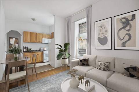 A living room with a grey couch, a dining table with chairs, and a kitchen area with cabinets and a fridge.