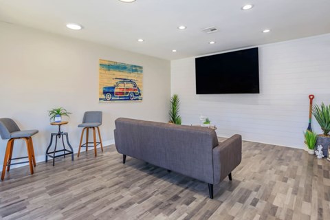 A living room with a grey couch, two chairs, a bar stool, a plant, and a painting on the wall.
