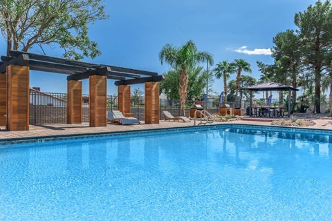 A pool surrounded by palm trees and a wooden pergola.