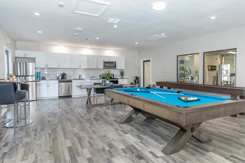 A pool table in a room with a kitchen in the background.