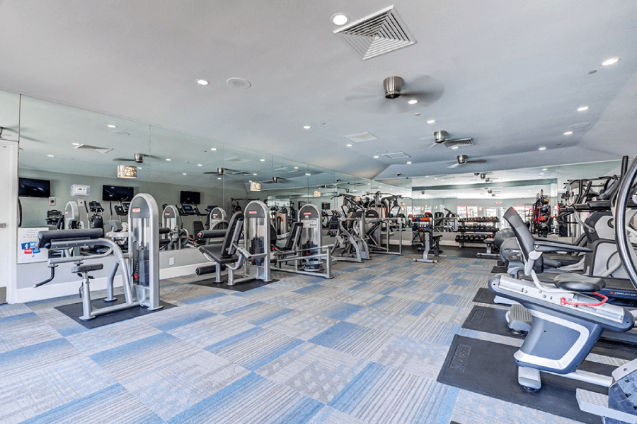 A gym with a variety of equipment including treadmills, weights, and exercise machines at Kirker Creek Apartments, Pittsburg 94565