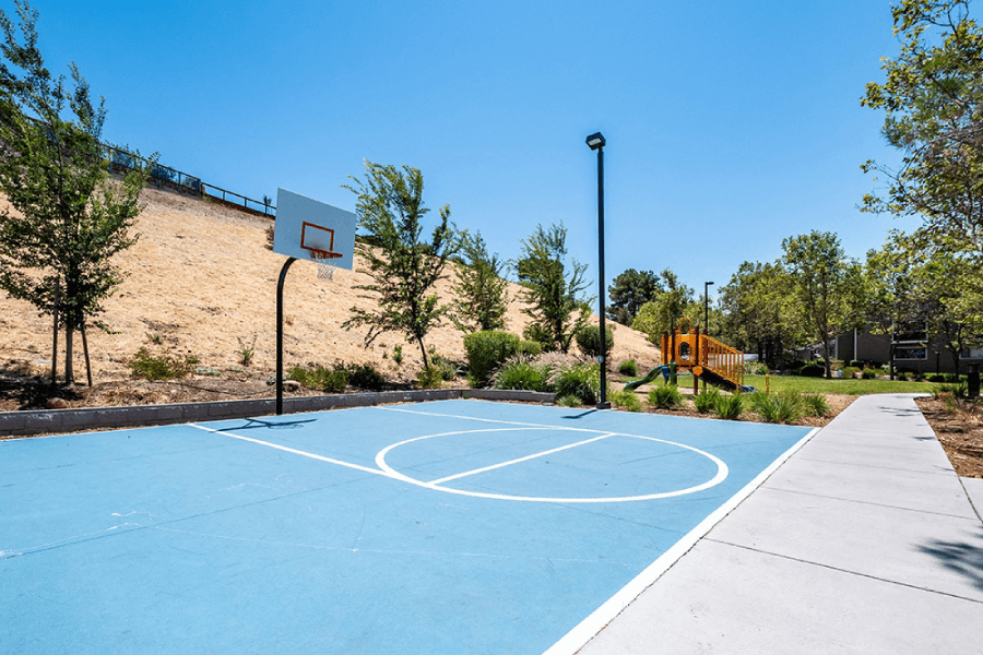A basketball court with a blue surface and white lines, surrounded by trees and a hill in the background at Kirker Creek Apartments, Pittsburg, CA