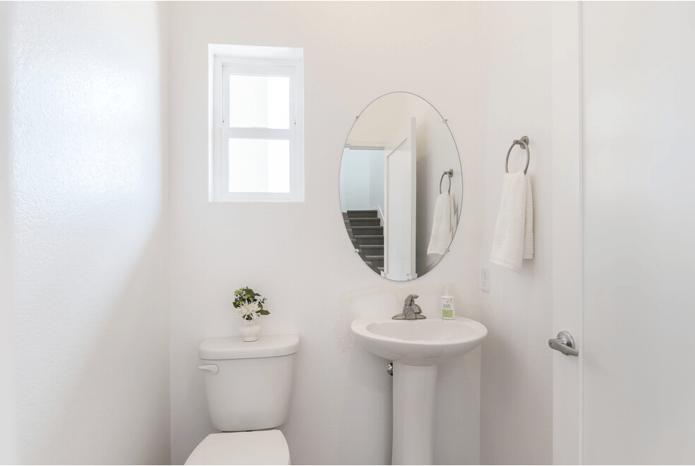 a white bathroom with a small window above the toilet and a white sink with a round mirror
