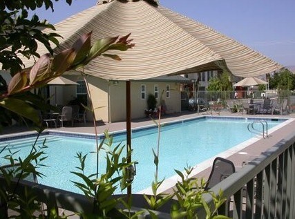 A pool under a shade structure with a building in the background.