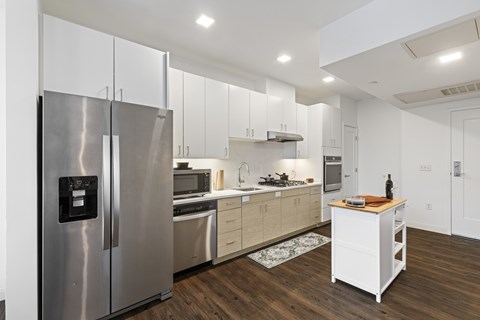 A modern kitchen with a stainless steel refrigerator and wooden flooring.