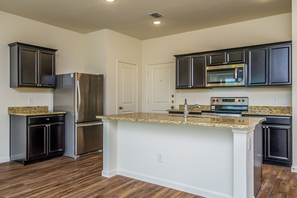 Forney TX Houses for Rent - Windmill Farms - Kitchen with Wood-Style Flooring, Beige Walls, Stainless Steel Appliances, Granite Countertops, Kitchen Island, and Dark Wood-Style Cabinets