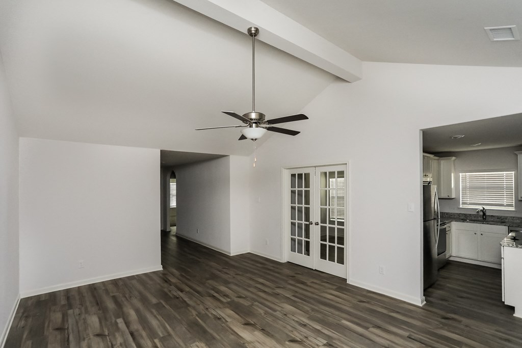 an empty living room with a ceiling fan and a kitchen
