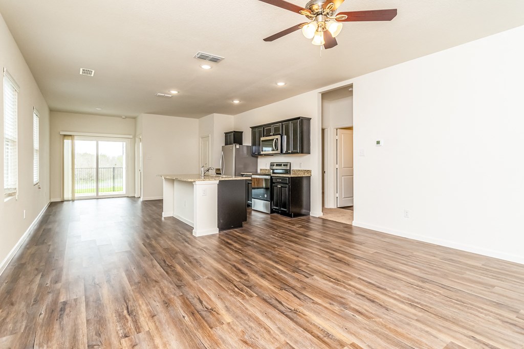 an empty living room with a kitchen and a ceiling fan