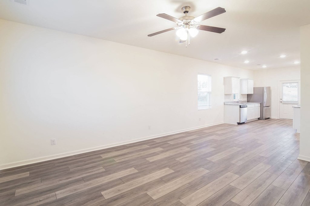an empty living room with a ceiling fan and a kitchen