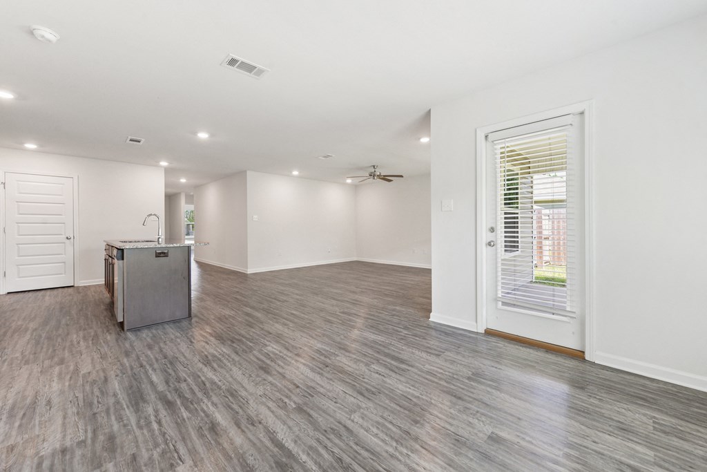 an empty living room with a kitchen and a large window