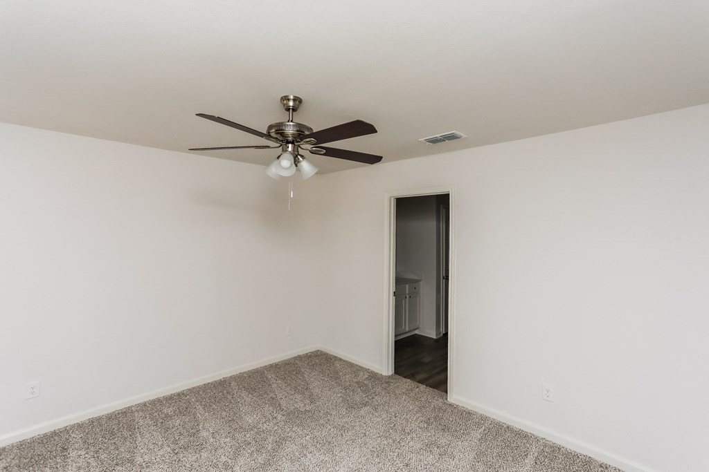 an empty room with a ceiling fan and a door to a hallway