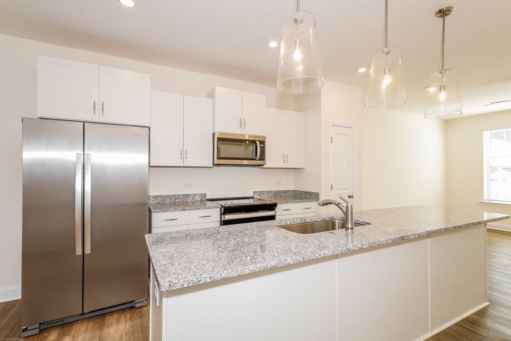 Townhouses for Rent in Charlotte, NC - Loso Walk - Modern Kitchen with Granite Countertops, a Kitchen Island, Hanging Lights, White Cabinetry, Stainless Steel Appliances, and Luxury Vinyl Plank Flooring