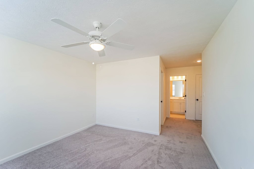 an empty living room with a ceiling fan and white walls