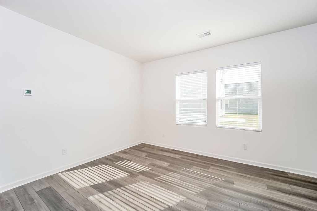 an empty room with wood flooring and two windows