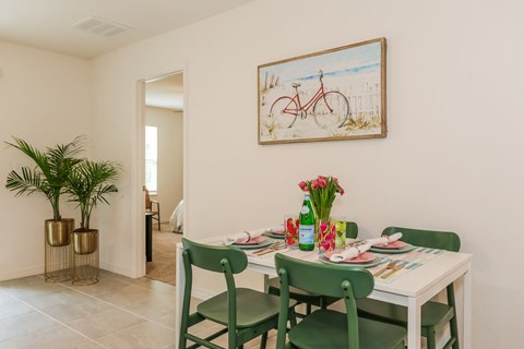 Dining room with a white table set for four, green chairs, tropical plants, and beach-themed artwork.