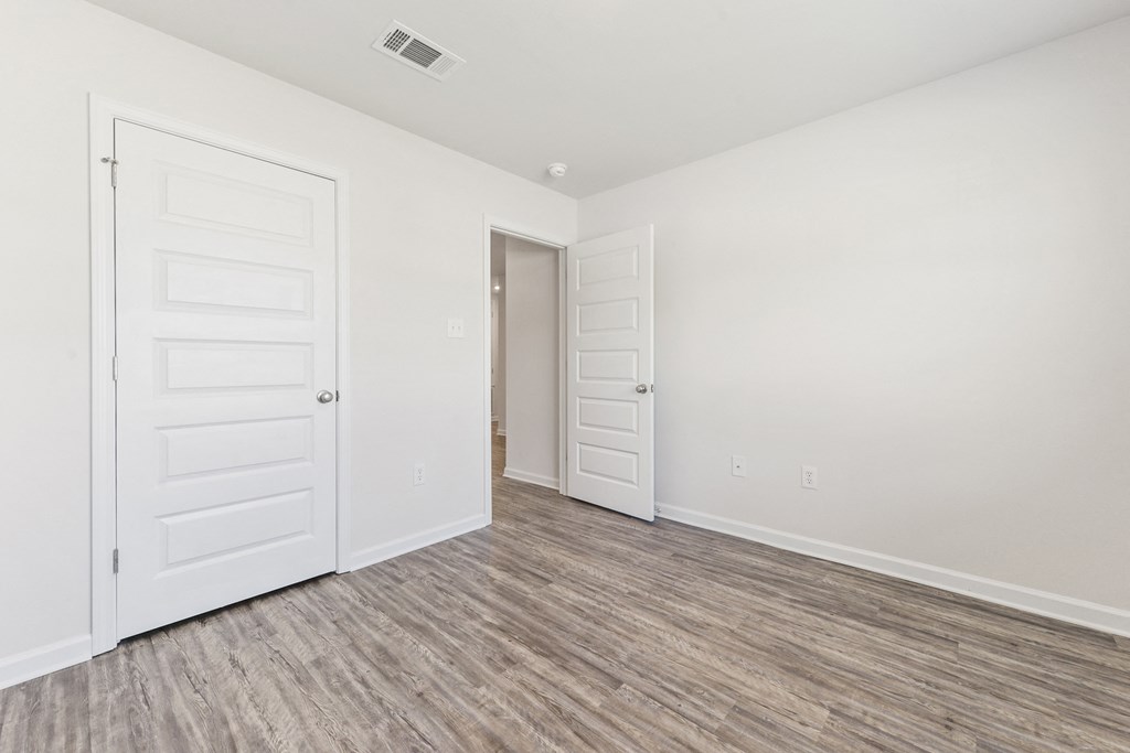 the living room and bedroom of a manufactured home with white walls and wood flooring