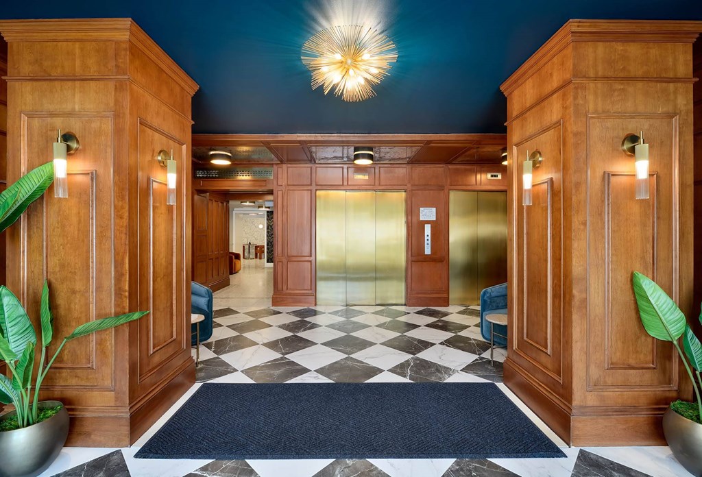 Elegant lobby with wood paneling, gold elevators, and black and white checkered marble floor.
