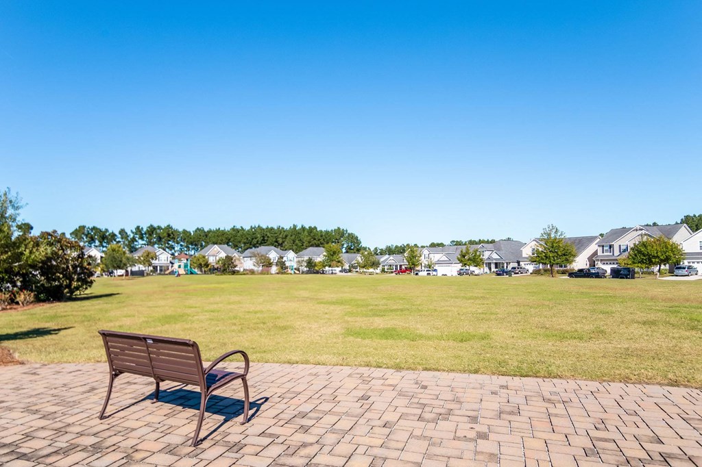 a park bench on a brick sidewalk next to a grass field