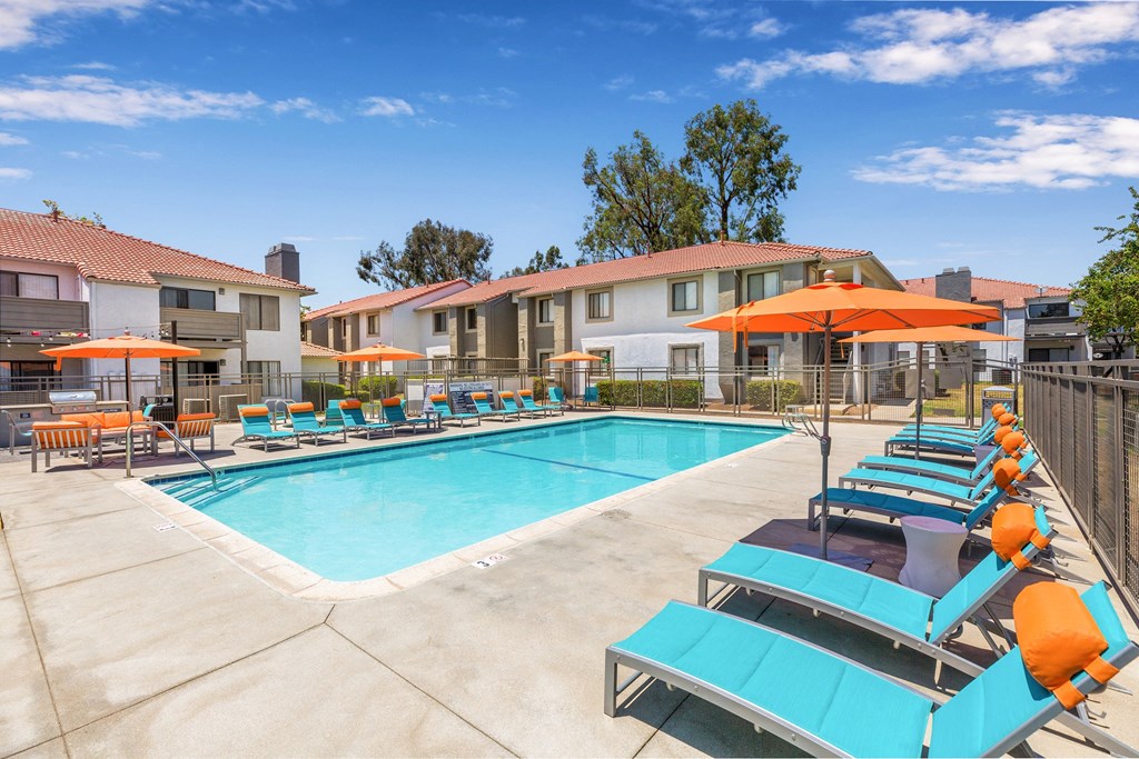 One-BR Apartments In Moreno Valley, CA - Gated Resort-Style Pool With Lounge Chairs, Tables, Chairs, Umbrellas, And BBQ Grill.